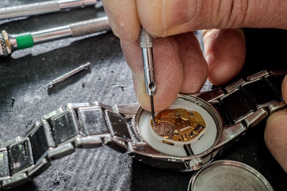 Des mains utilisent un tournevis de précision pour réparer une montre-bracelet en argent, le boîtier étant ouvert.