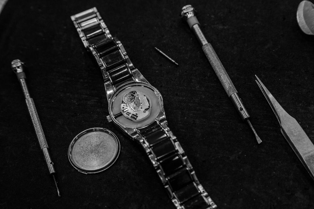 Des outils de réparation de montres disposés autour d'une montre-bracelet ouverte sur une surface sombre