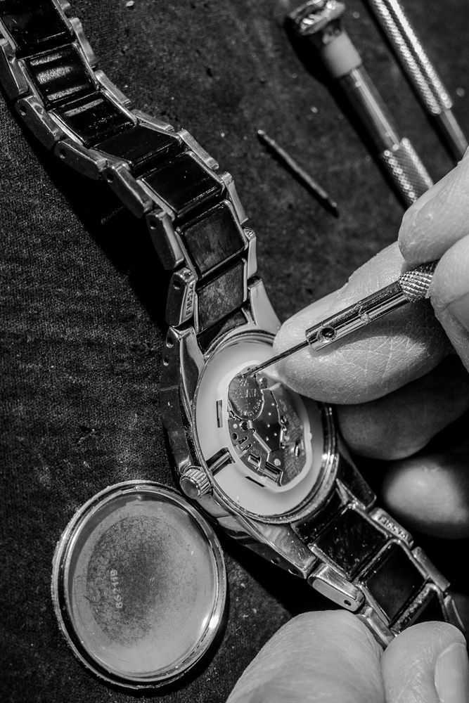 Gros plan sur la réparation d'une montre : une main utilise un outil pour ajuster le boîtier et le bracelet ouverts.