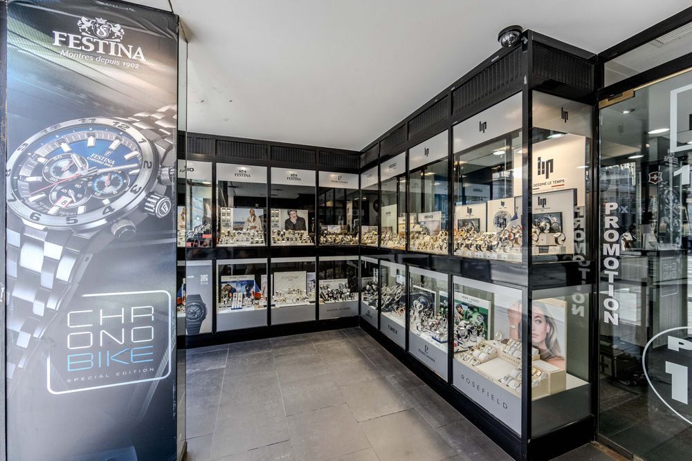 Une vitrine de magasin de montres avec des vitrines, une bannière publicitaire et un trottoir.