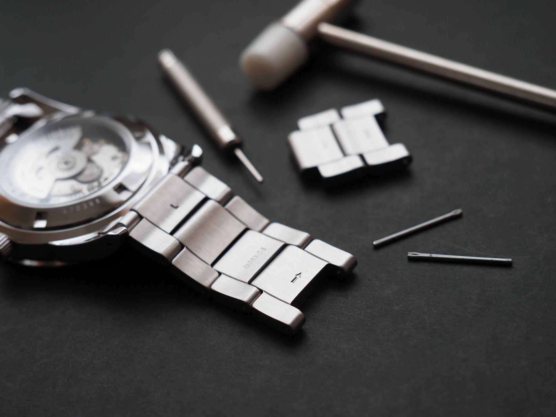 Bracelet de montre ajusté avec des outils sur une surface sombre.