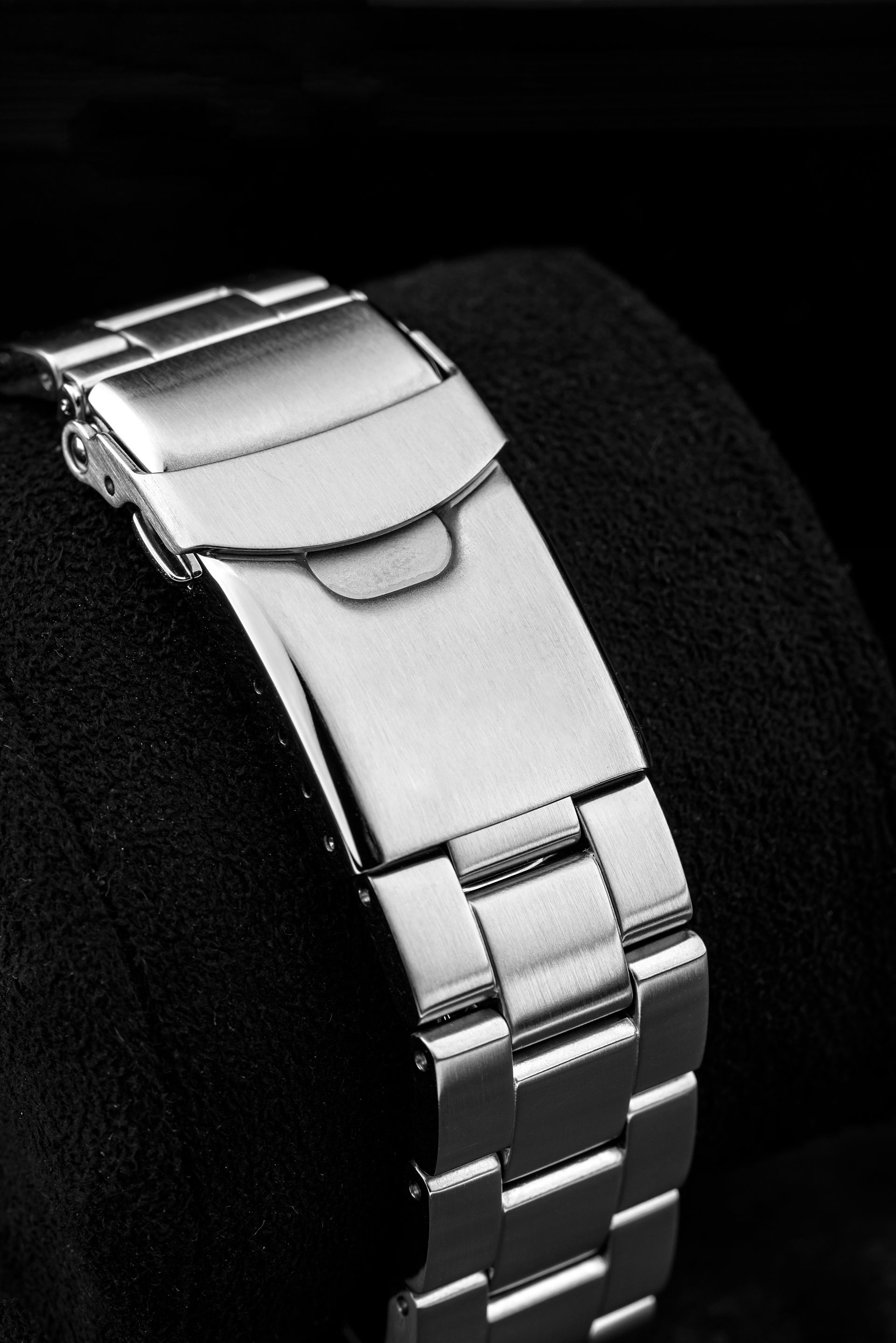 Fermoir de bracelet de montre en acier inoxydable, gros plan sur un fond sombre.