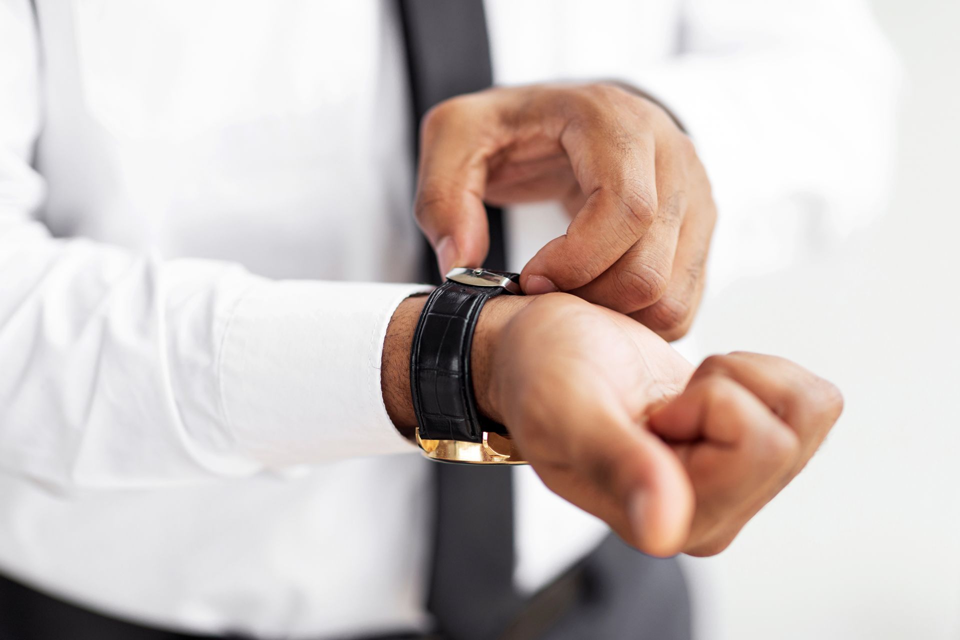 Homme en chemise blanche et cravate ajustant une montre noire et or.