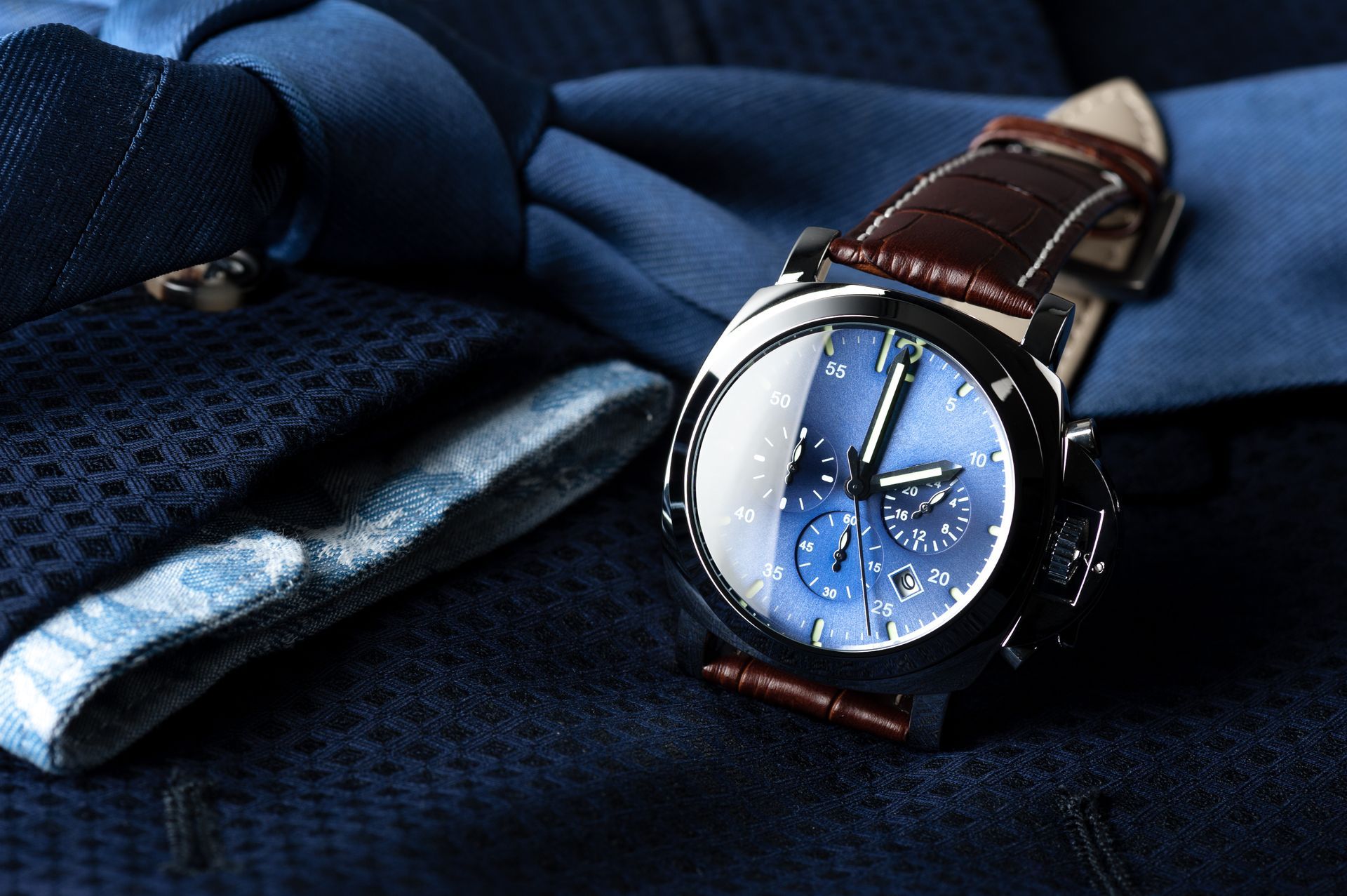 Montre bleue avec bracelet en cuir marron sur costume bleu avec cravate.