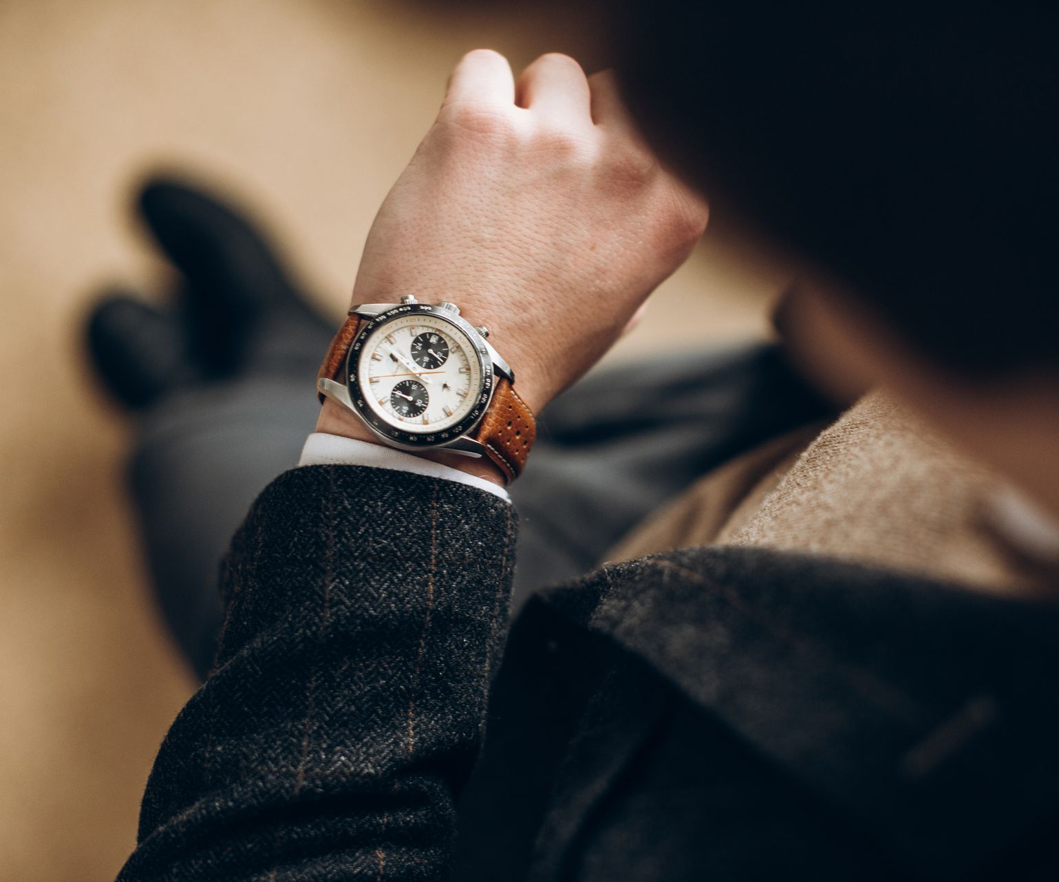 Homme regardant une montre-bracelet avec un bracelet en cuir marron, portant une veste en tweed.