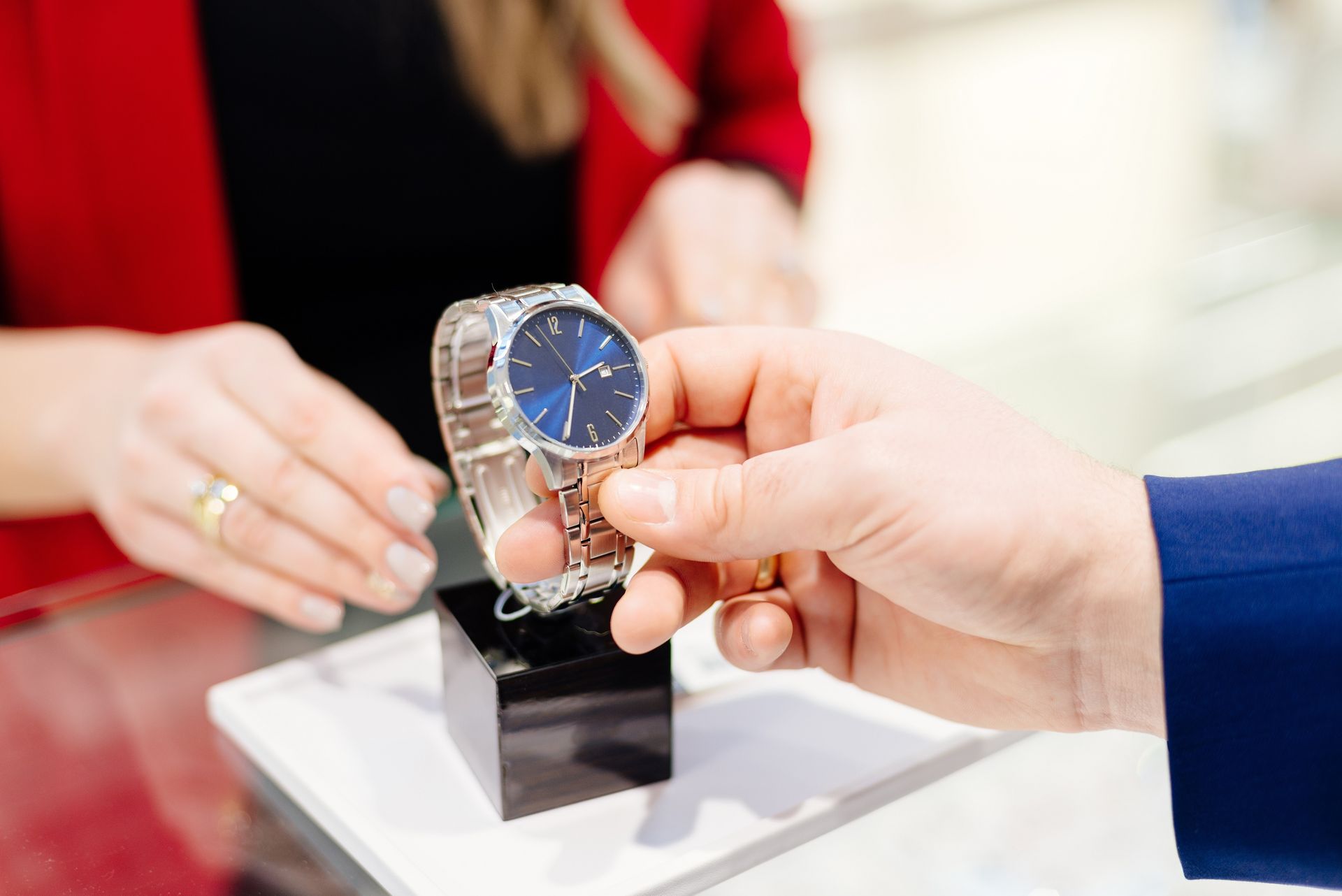 Une personne tend une montre-bracelet en argent avec un cadran bleu à un client dans une bijouterie.