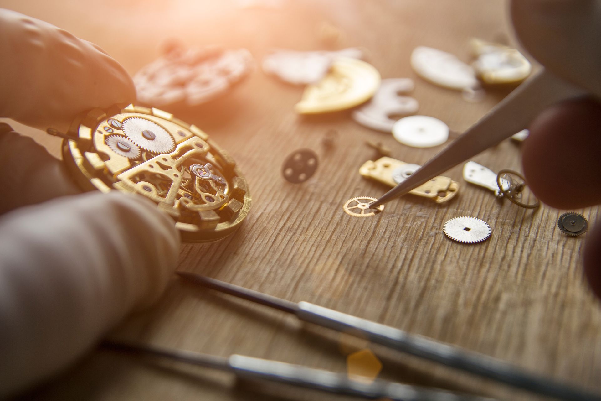 Mains avec des outils réparant un mécanisme de montre sur une surface en bois.