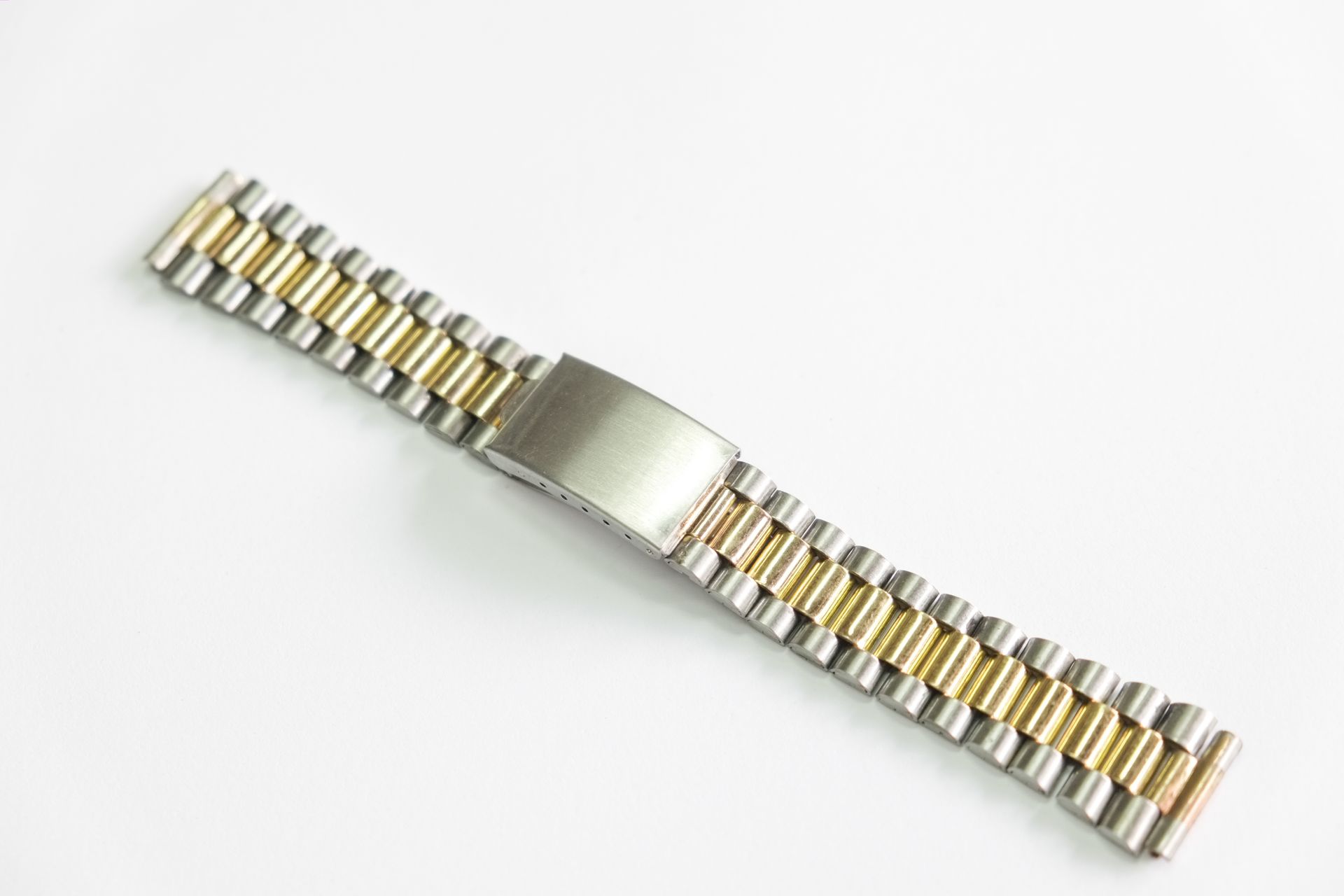 Bracelet de montre en métal bicolore, maillons argent et or, fermoir argent, posé sur surface blanche.
