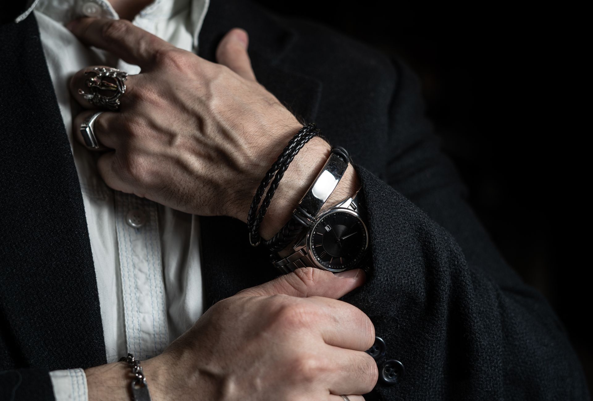 Un homme en costume ajuste sa manche, portant une montre, des bagues et des bracelets.
