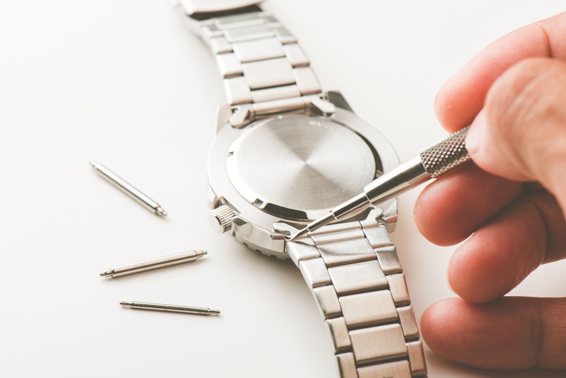Une personne ajuste un bracelet de montre en métal avec un tournevis sur une surface blanche.