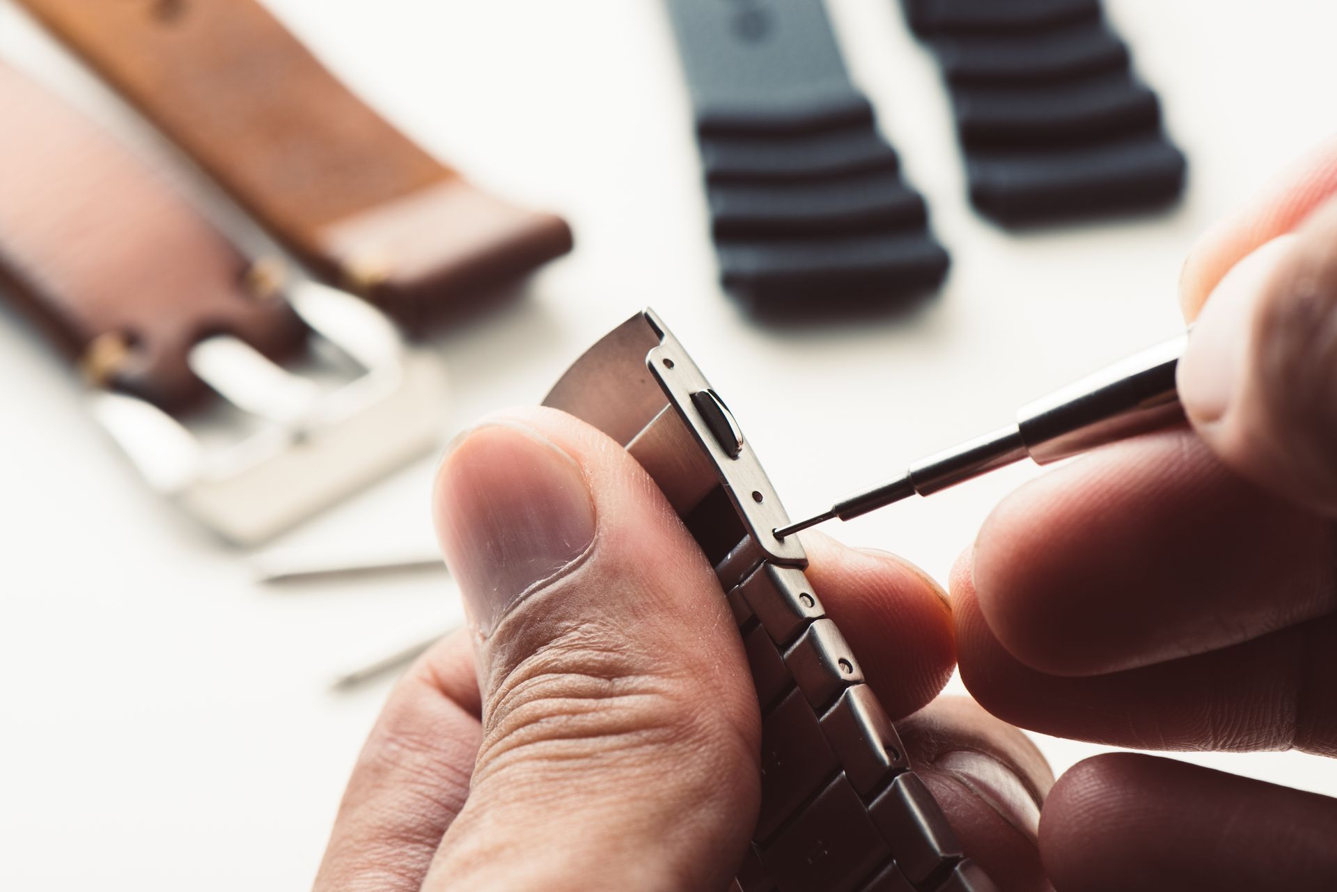 Personne utilisant un outil pour ajuster un bracelet de montre, avec d'autres bracelets et outils visibles.