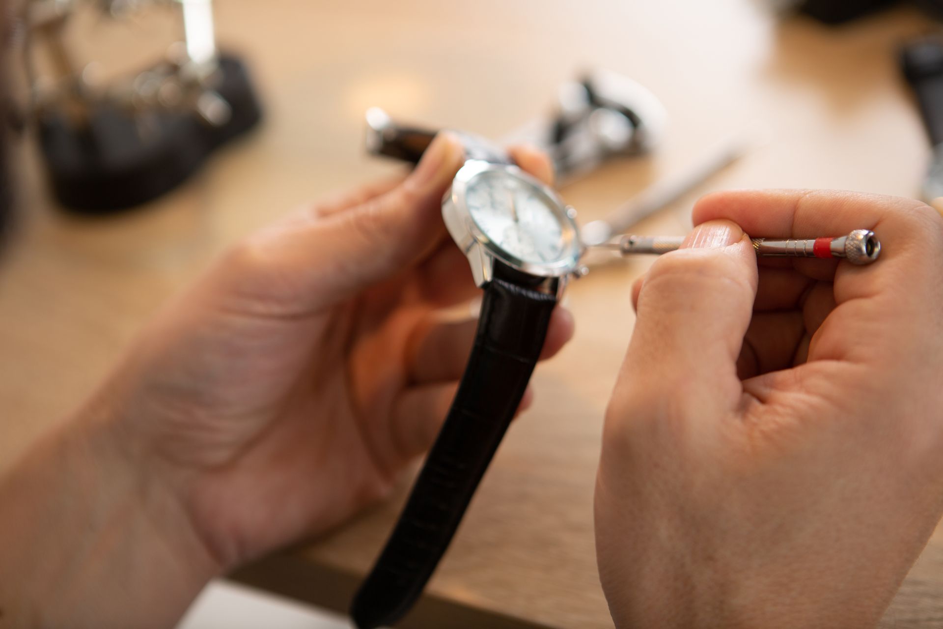 Personne réparant une montre-bracelet avec un petit tournevis sur une surface en bois.