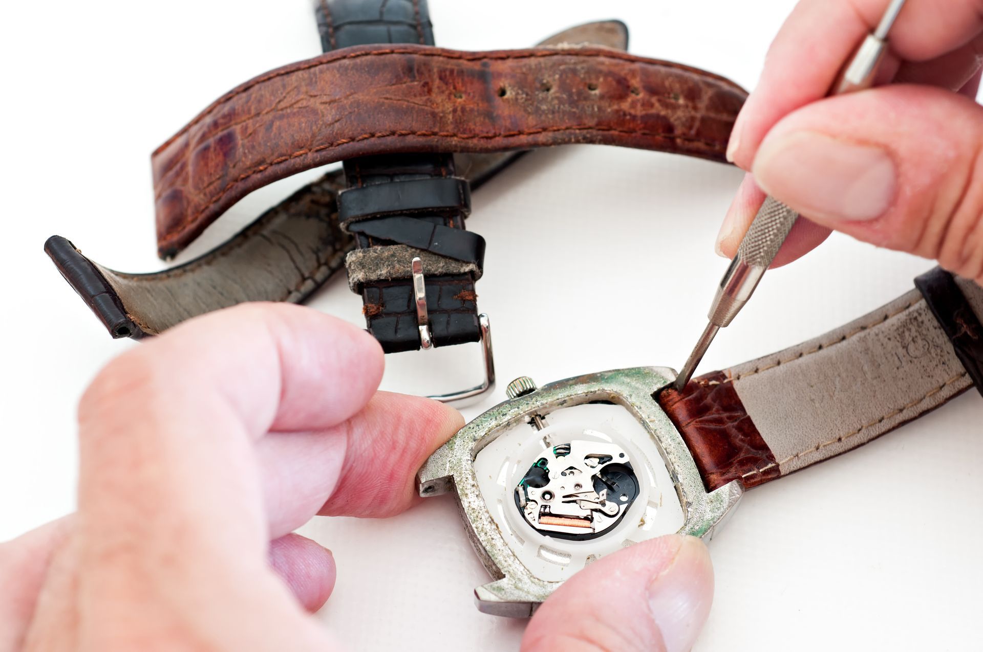 Personne utilisant une pince à épiler pour retirer un bracelet de montre, fond blanc.