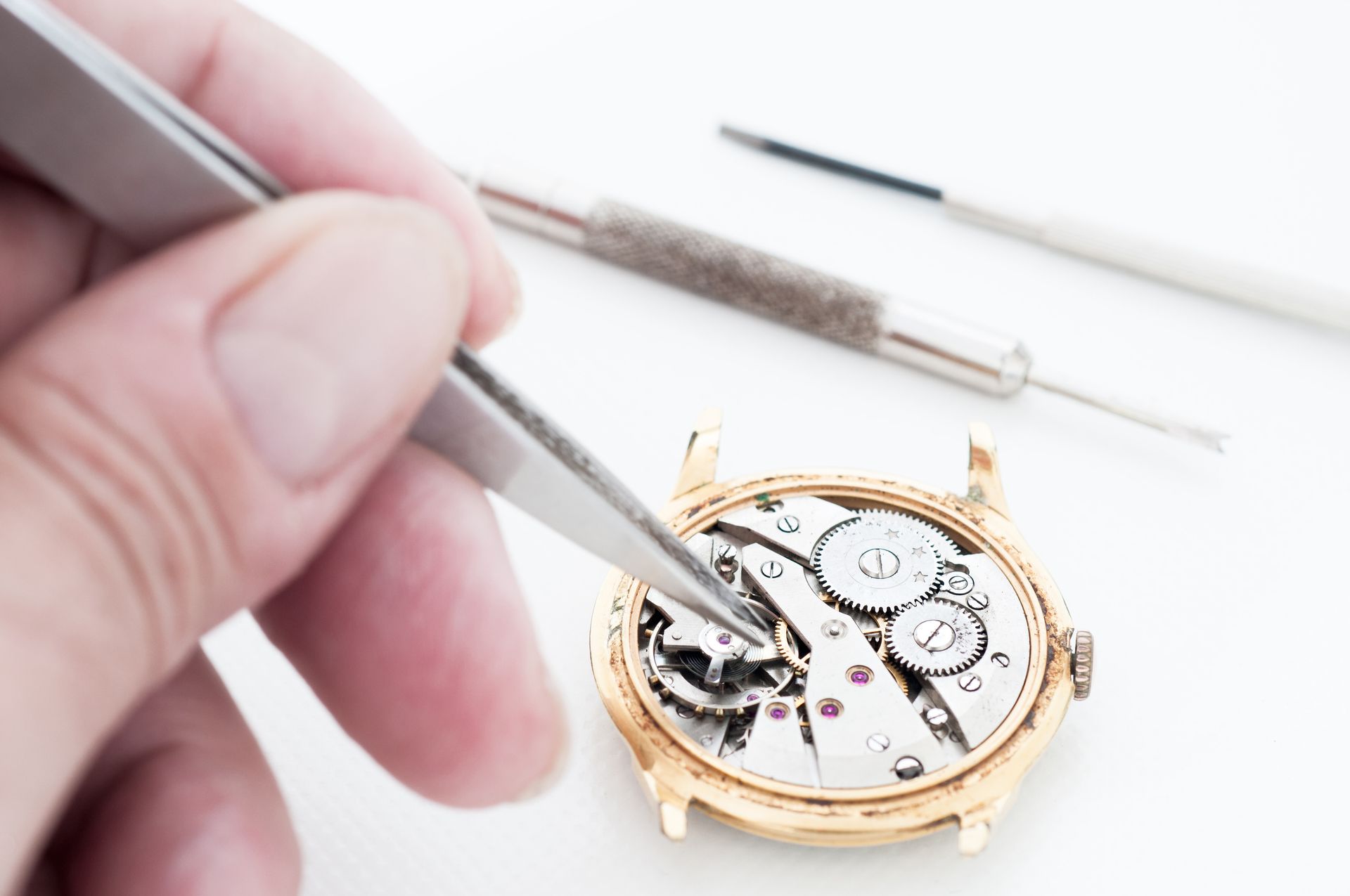 Une personne utilisant une pince à épiler pour réparer le fonctionnement interne d'une montre-bracelet en or.
