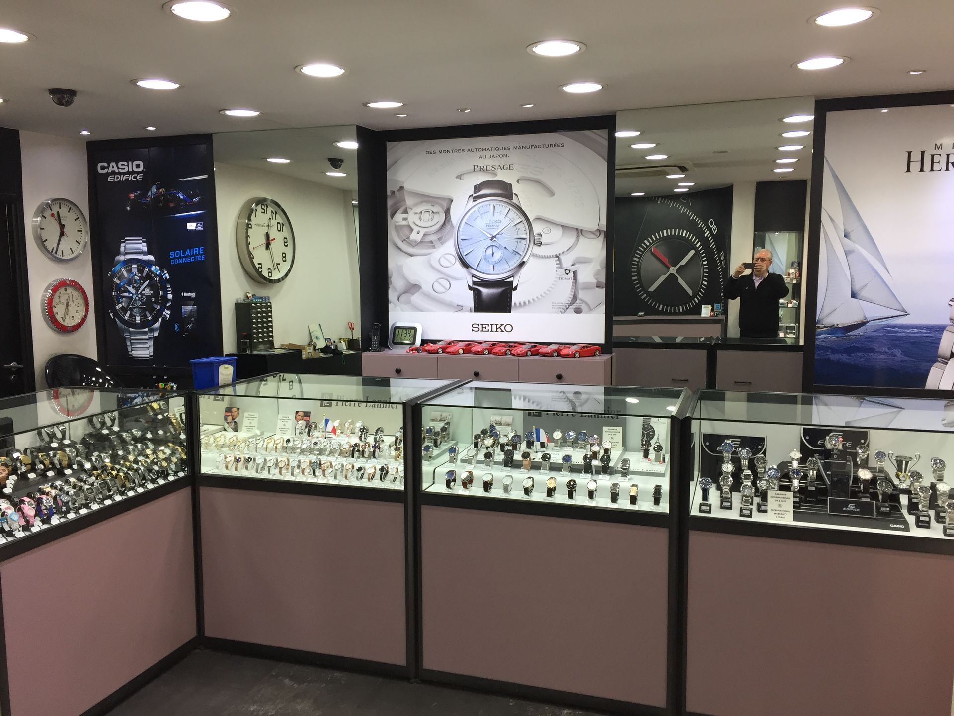 Intérieur d'un magasin de montres avec vitrines remplies de montres. De grandes affiches de montres sont accrochées aux murs.