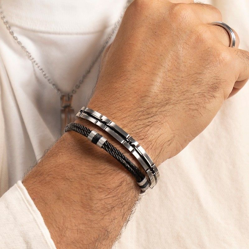 Poignet d'homme orné de deux bracelets argent et noir, portant une bague.