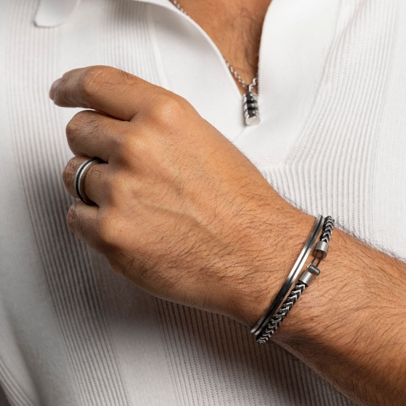 Bras d'homme avec bracelets et bague en argent, vêtu d'un polo blanc, main sur la poitrine.
