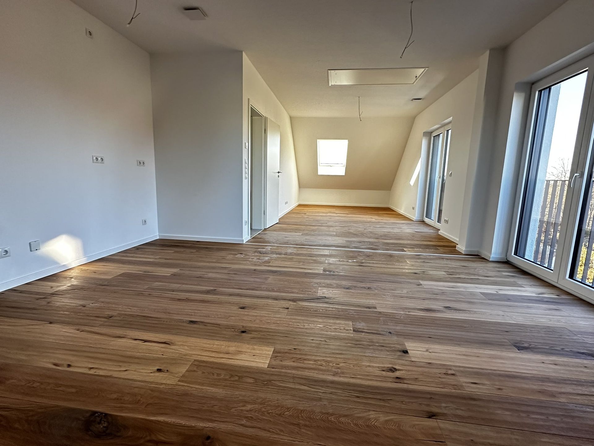 Leerer Raum mit Hartholzböden, weißen Wänden und großen Fenstern.