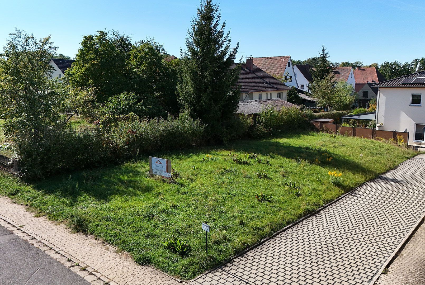 Draufsicht auf einen rechteckigen Hof mit einer Hecke, einem kleinen Baum und einem Gebäude, neben dem ein Auto geparkt ist.