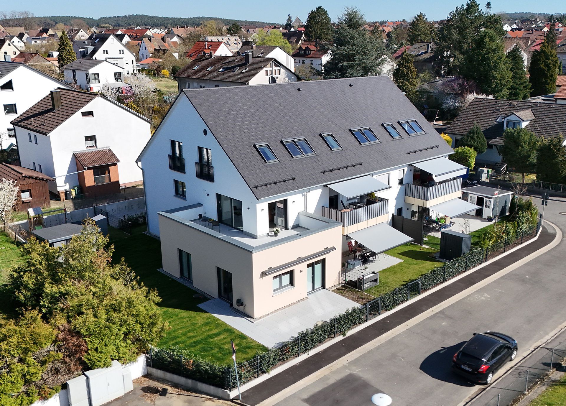 Modernes weißes mehrstöckiges Haus mit grauem Dach, kleinen Balkonen und gepflastertem Hof.
