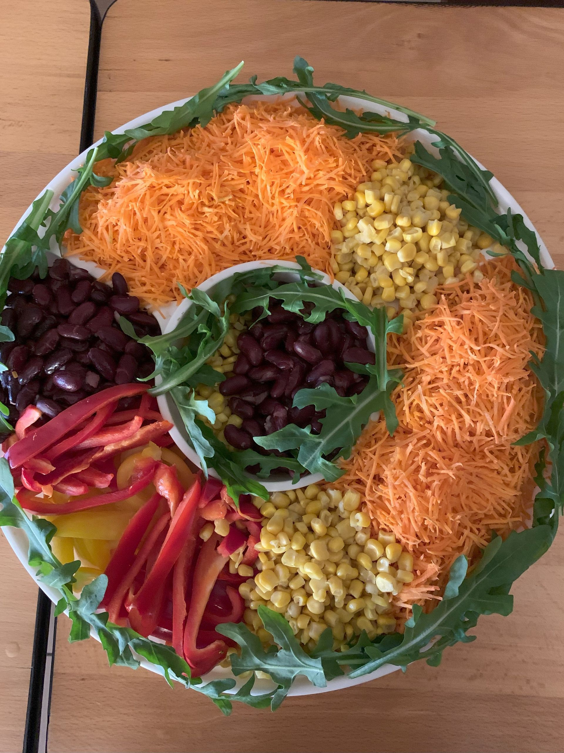 Bunte Platte mit schwarzen Bohnen, geraspelten Karotten, Mais, Paprika und Rucola.