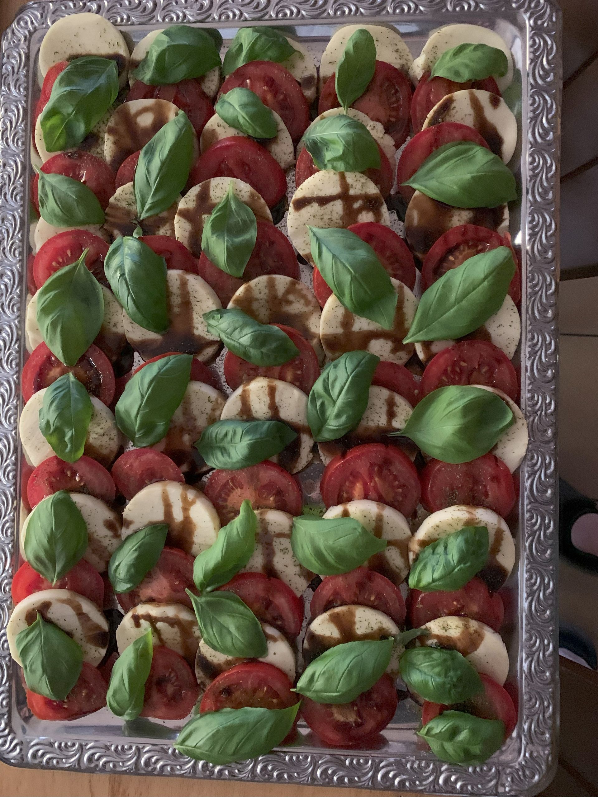 Caprese-Salat auf einem Silbertablett: Tomate, Mozzarella, Basilikum, beträufelt mit Balsamico-Glasur.