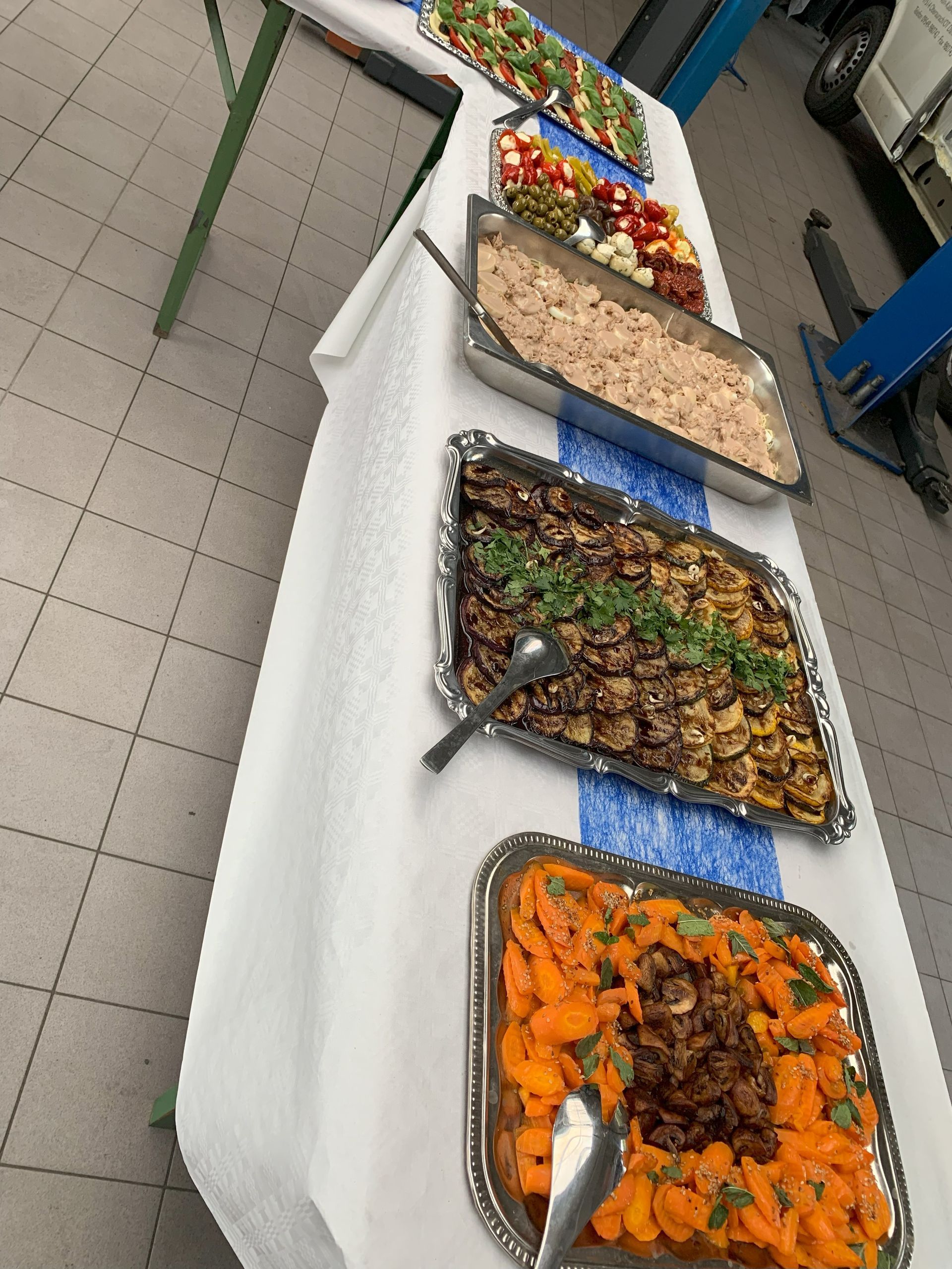 Buffettisch mit verschiedenen Gerichten, darunter Karotten, Pilze und Salat, im Innenbereich, wahrscheinlich bei einer Veranstaltung.