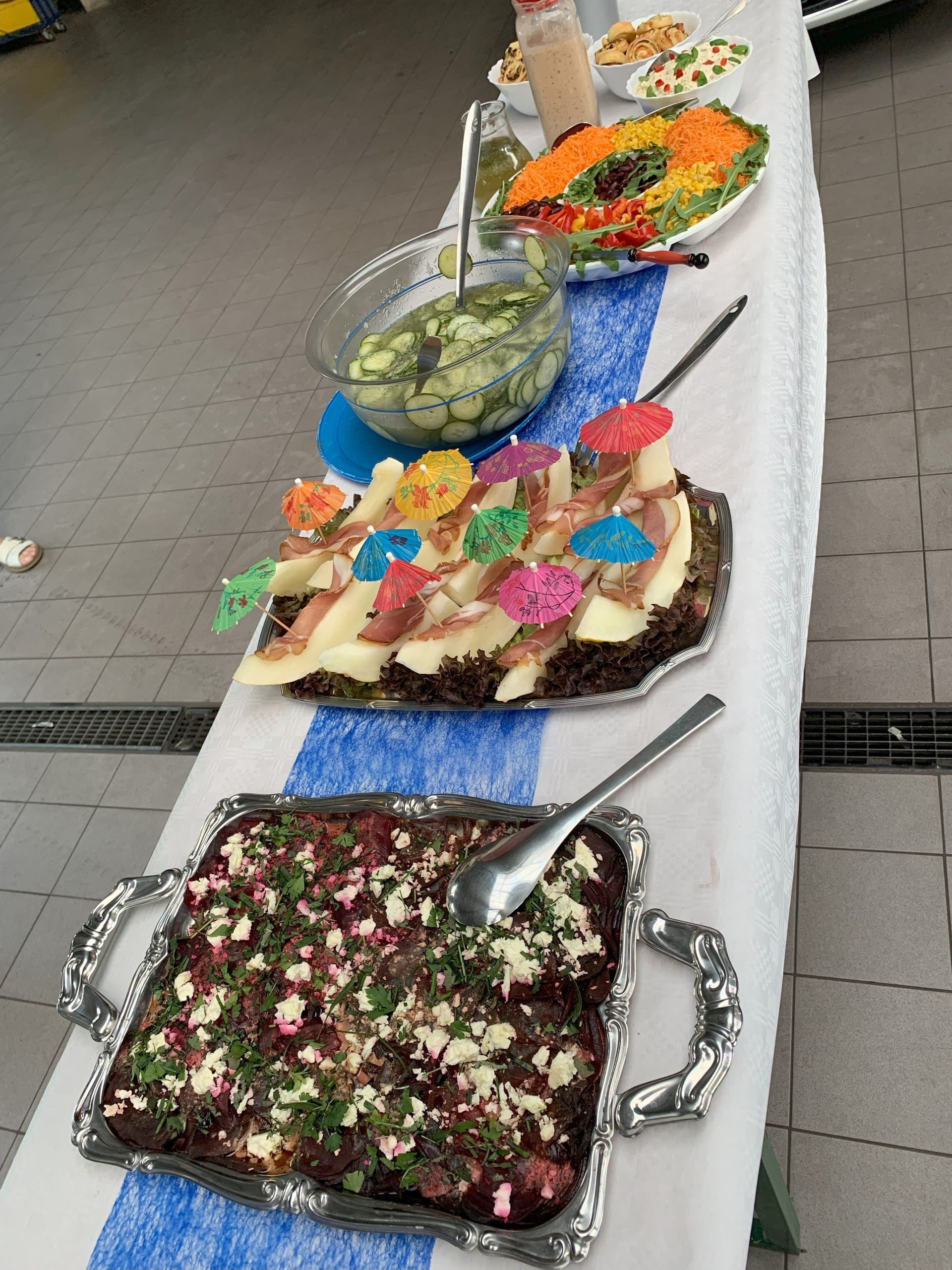 Buffettisch mit mehreren Salaten und einem Dessert, dekoriert mit bunten Cocktailschirmchen.