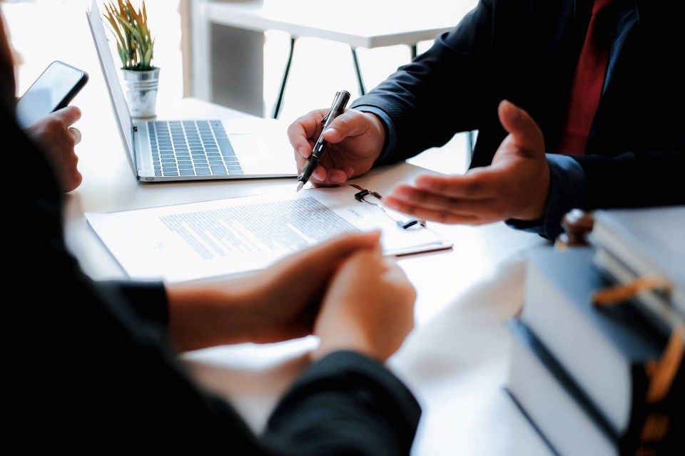 Vertrag auf Klemmbrett, Personen an Tisch gegenüber