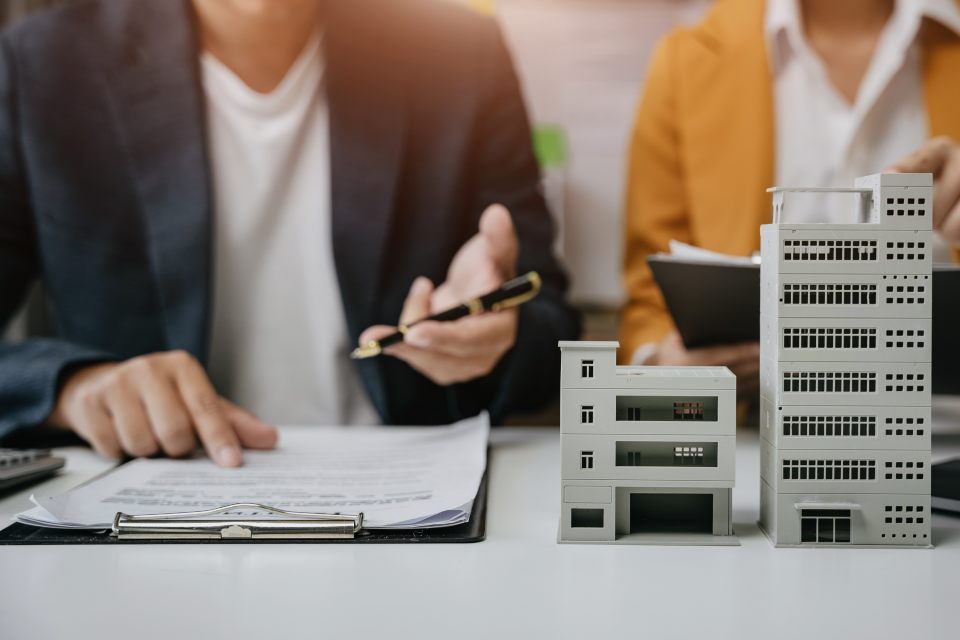 Person and Schreibtisch mit Hausmodell und Klemmbrett mit Dokument