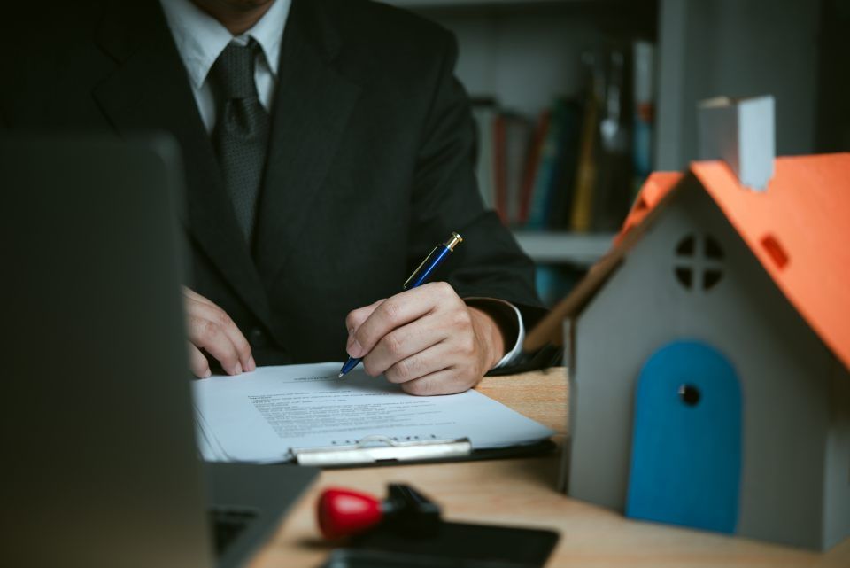 Person, Schreibtisch mit Hausmodell und Klemmbrett mit Dokument