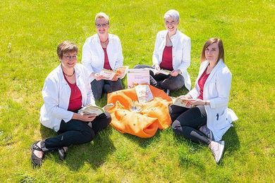 Vier Mitarbeiterinnen der Aesculap Apotheke Christa Kahle e.K. sitzen auf Gras