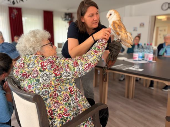 Woman holding an owl while seated woman reaches out in a bright indoor room
