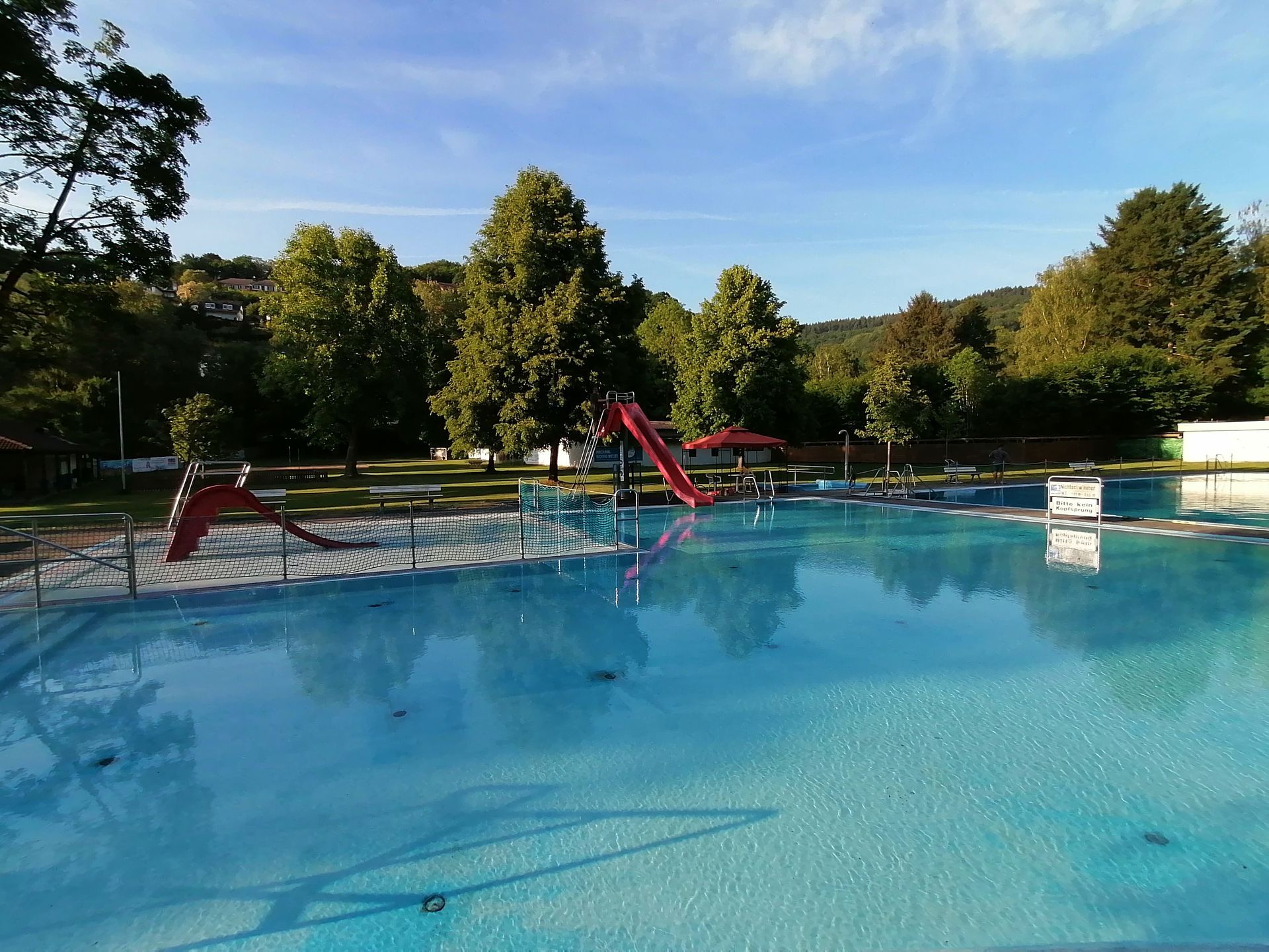 Freibad zur Wartung abgelassen, blaue Oberfläche und rote Reinigungsgeräte unter sonnigem Himmel