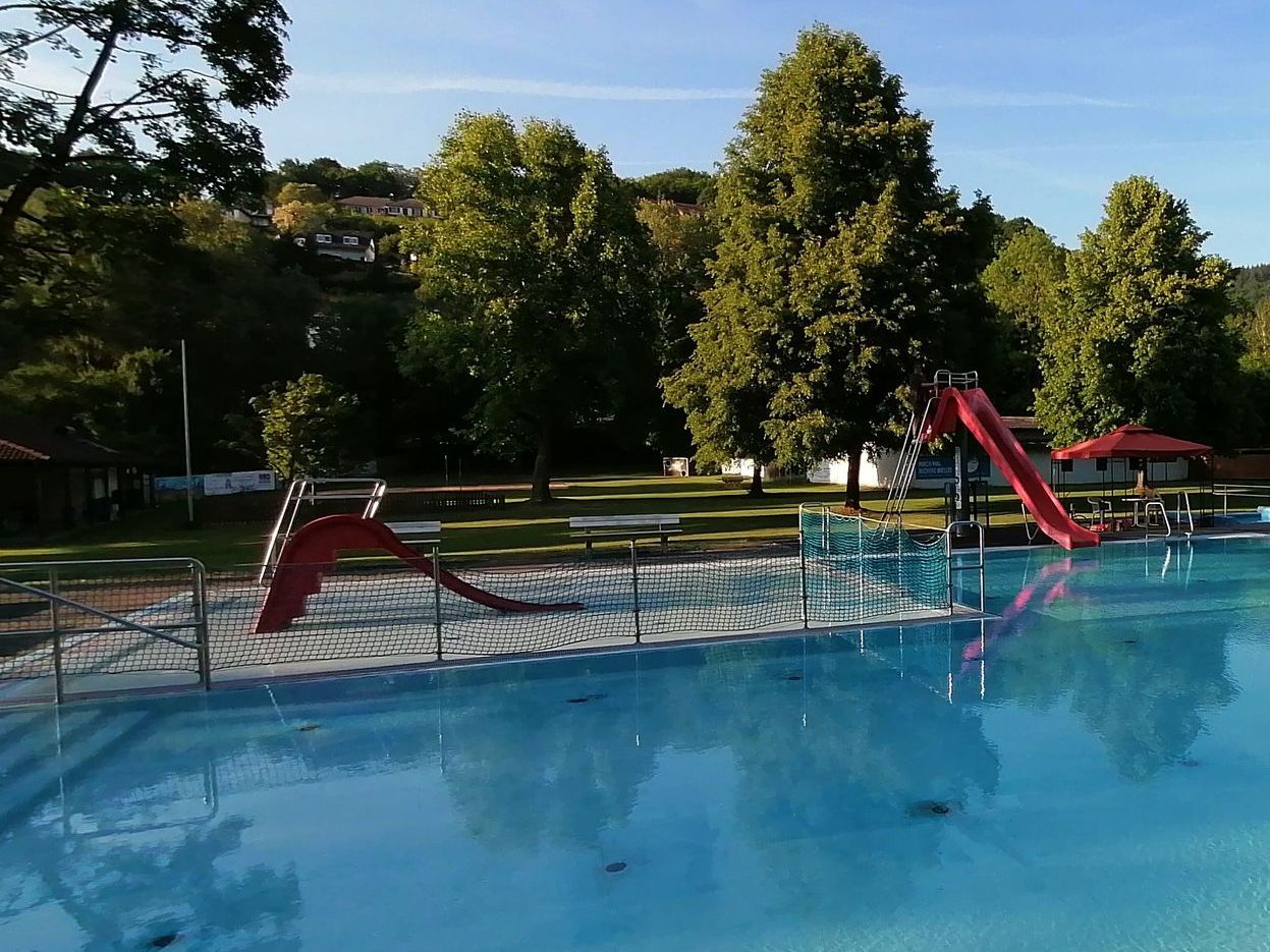 Ein Panoramabild des Freibades Oberbieber. Eine Wiese links, eine rote Rutsche in der Mitte und mehrere Schwimmbecken rechts.