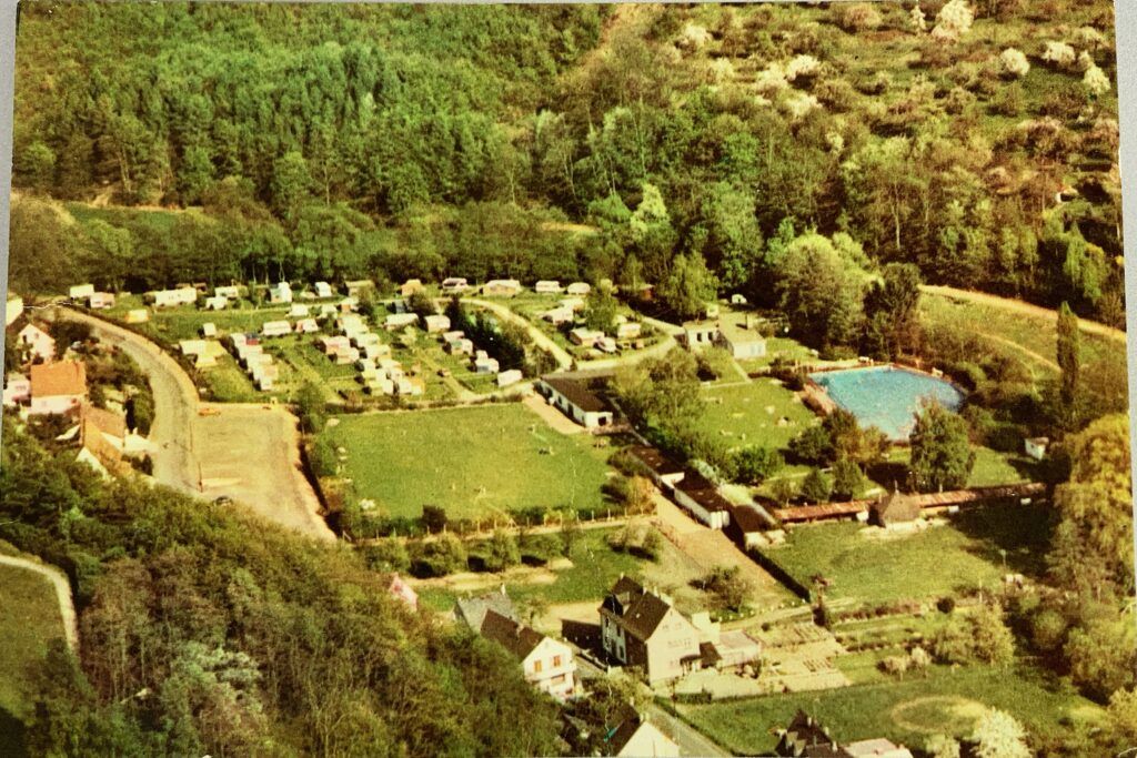 Eine Lufaufnahme eines Campingplatzes im Randgebiet eines Ortes, mit einem Freibad.