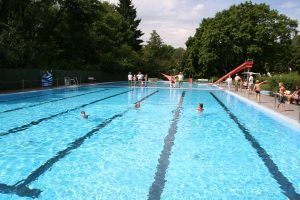 Ein Schwimmerbecken eines Freibades mit einer roten Rutsche im Hintergrund.