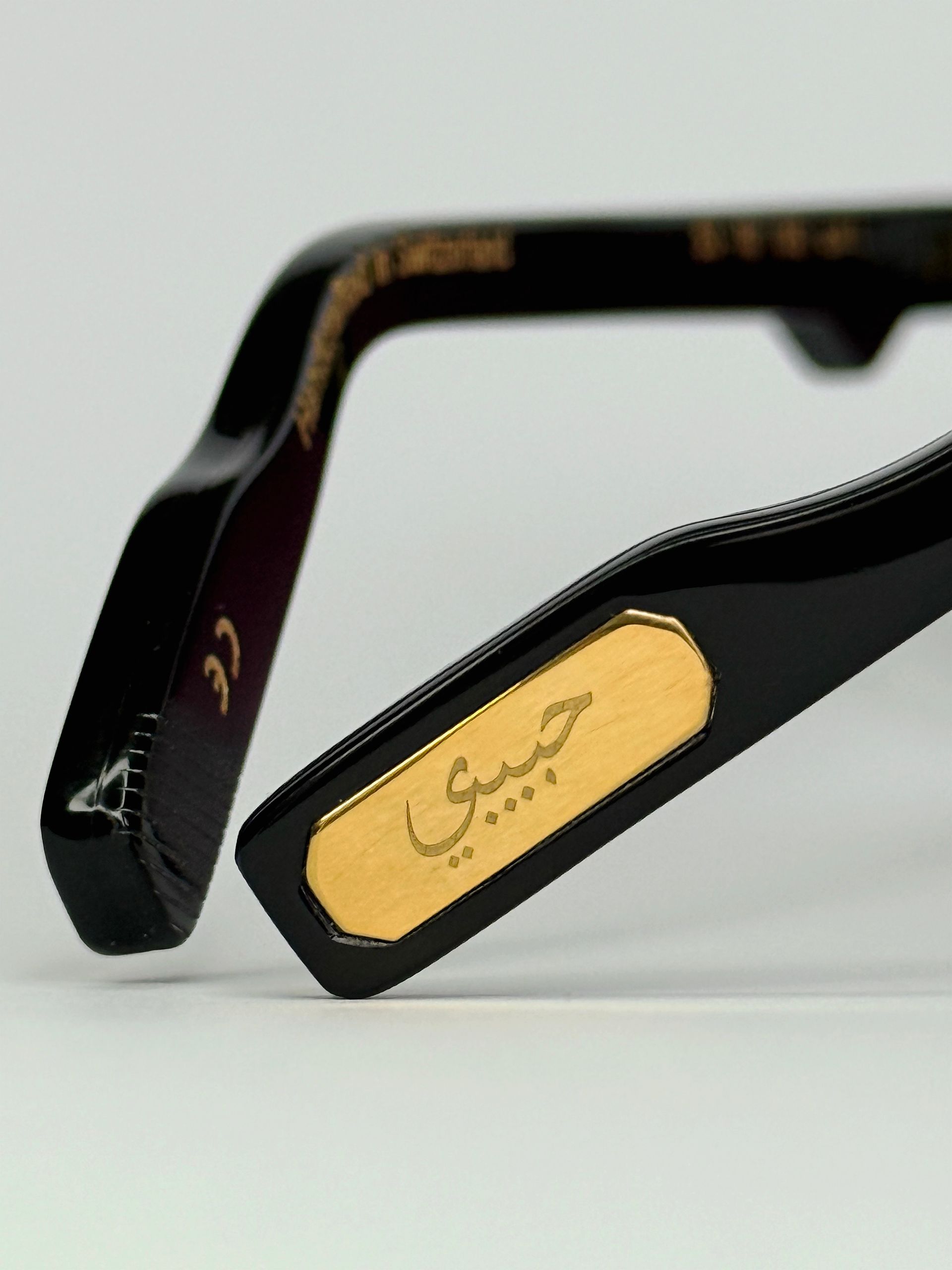 Schwarze Sonnenbrille mit goldener arabischer Schrift „habibi“ auf dem Rahmen, rosa Gläser.
