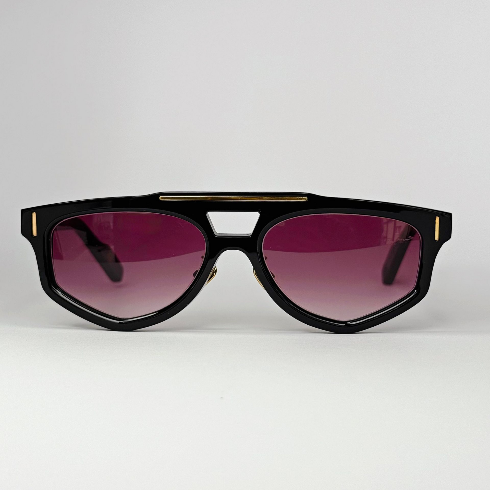 Schwarze Sonnenbrille mit goldenem Streifen oben und rosa-violetten Verlaufsgläsern.
