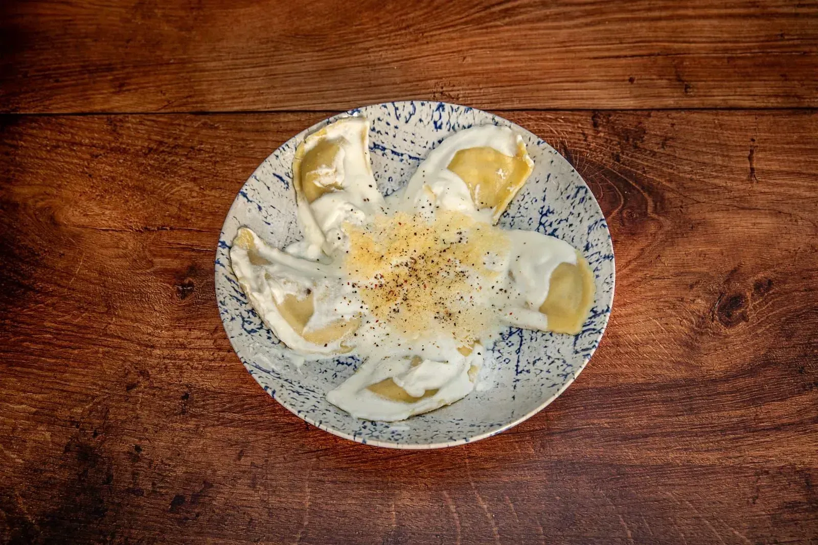 Plato de pierogis cubiertos de salsa, espolvoreados con pimienta, sobre una mesa de madera.