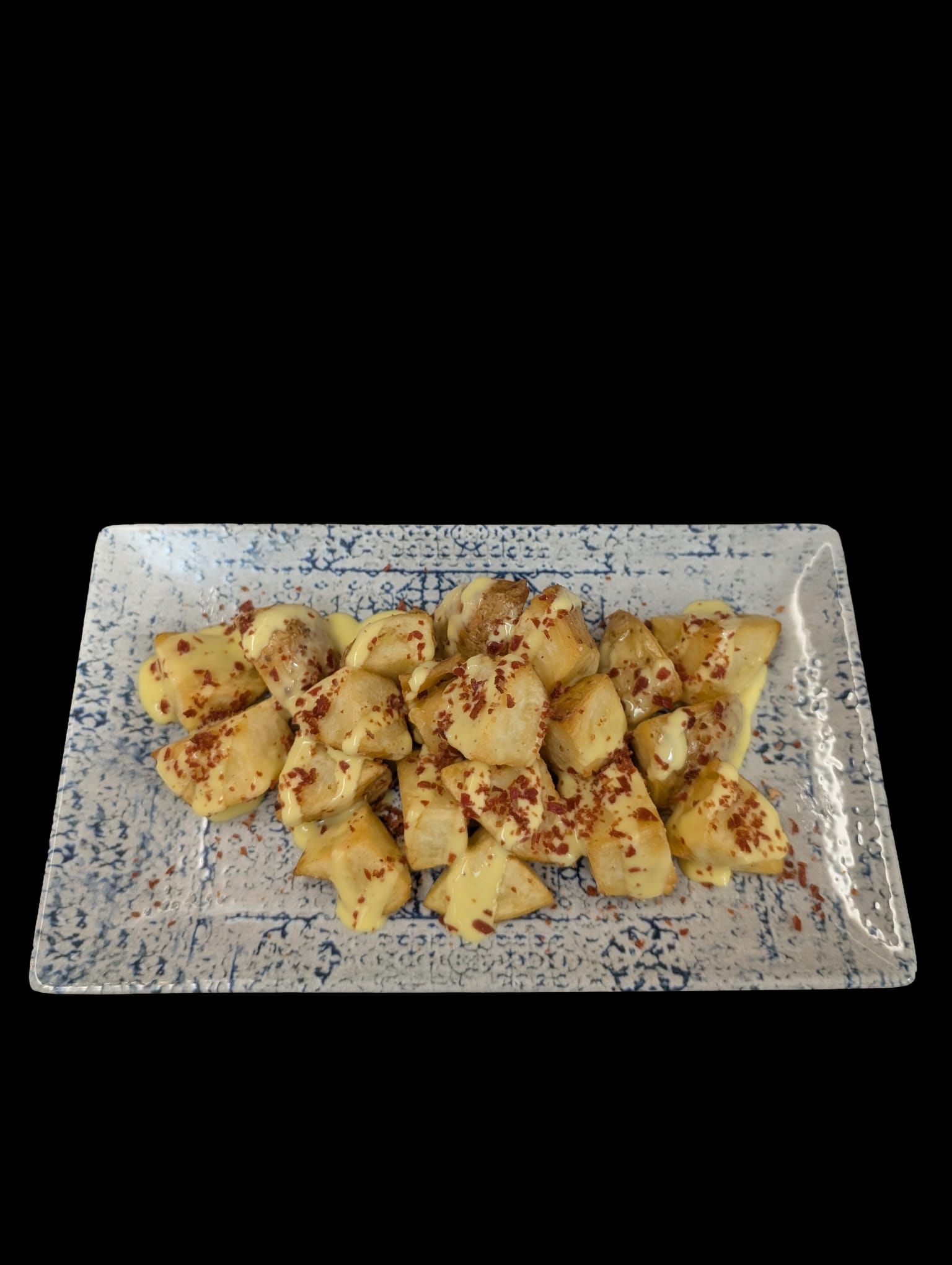 Patatas cocidas en un plato rectangular con dibujos, espolvoreadas con copos rojos y sobre un fondo negro.