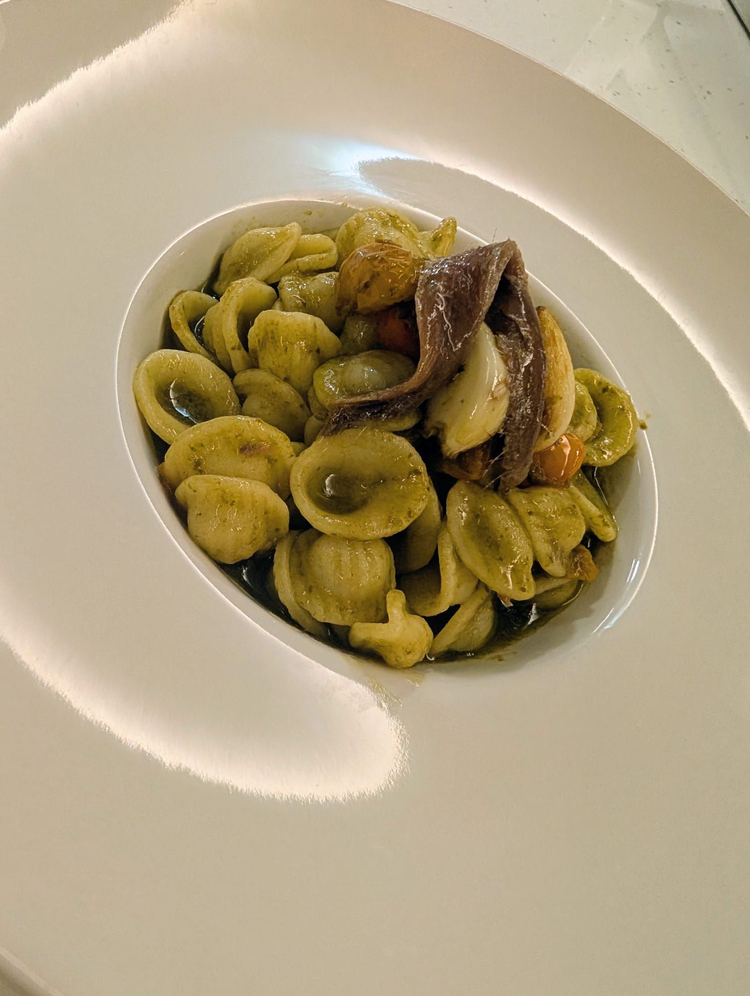 Plato de pasta orecchiette con pesto, anchoas y tomates en un bol blanco.