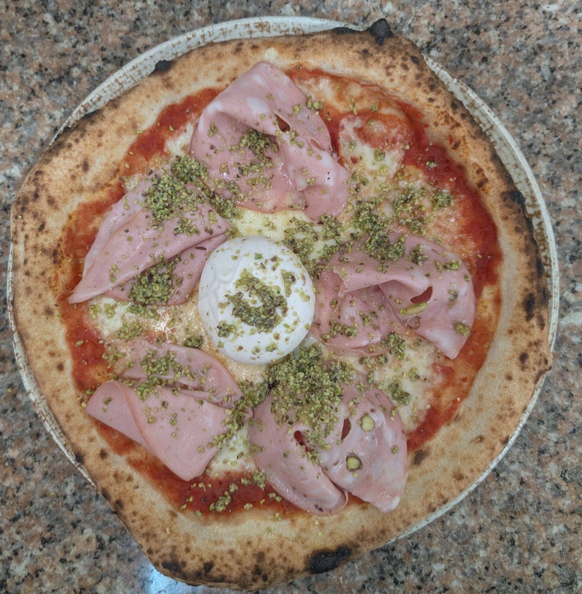 Pizza con mortadela, burrata y pistacho, en plato.