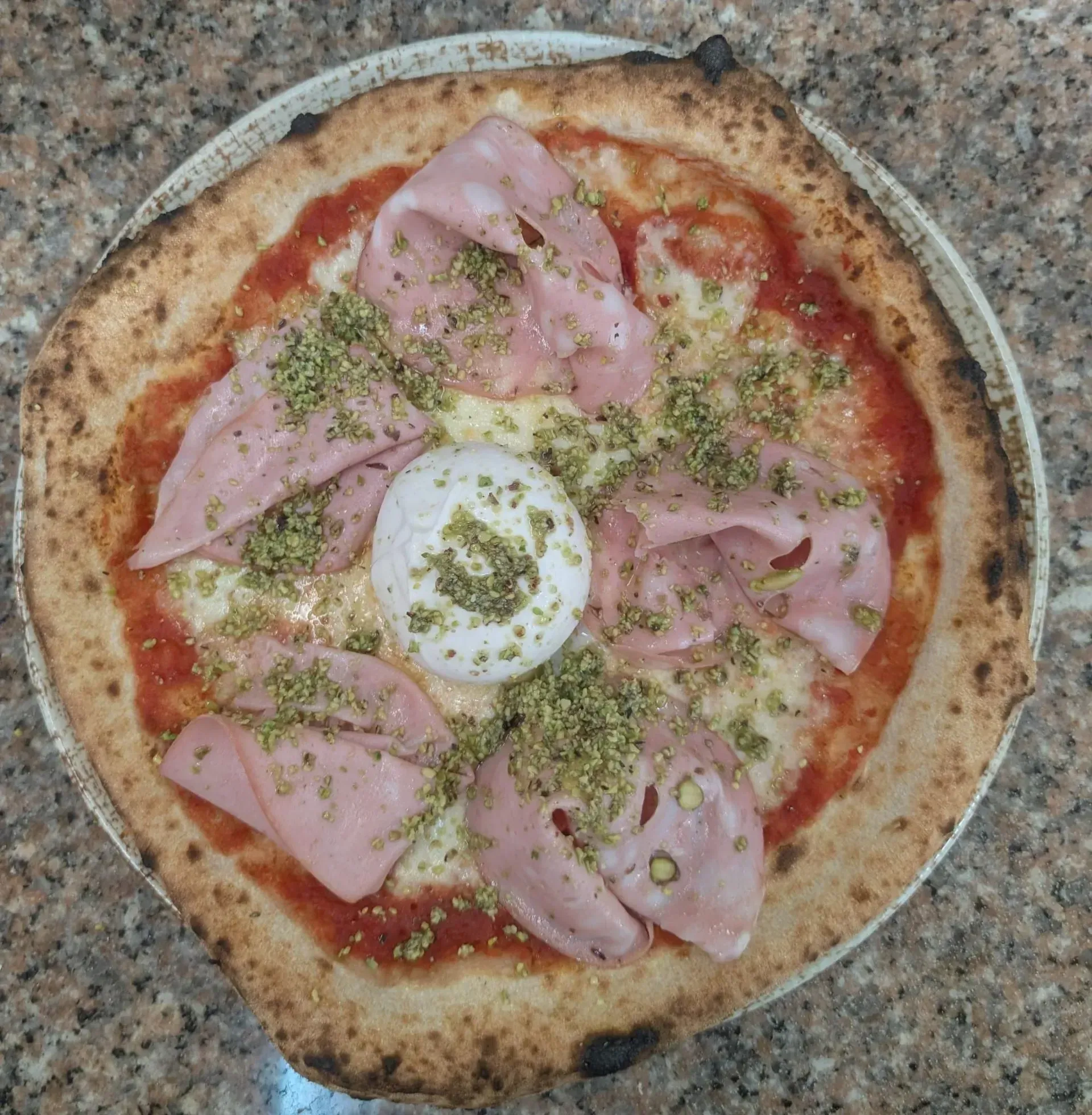 Pizza con mortadela, burrata y crumble de pistachos en un plato.