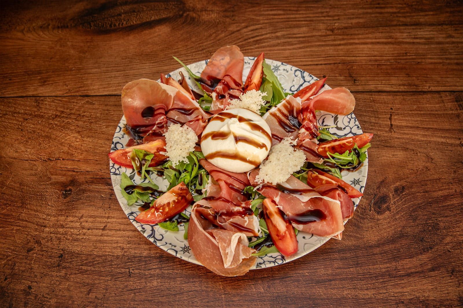 Plato de embutidos con prosciutto, burrata, tomates, rúcula y glaseado balsámico.