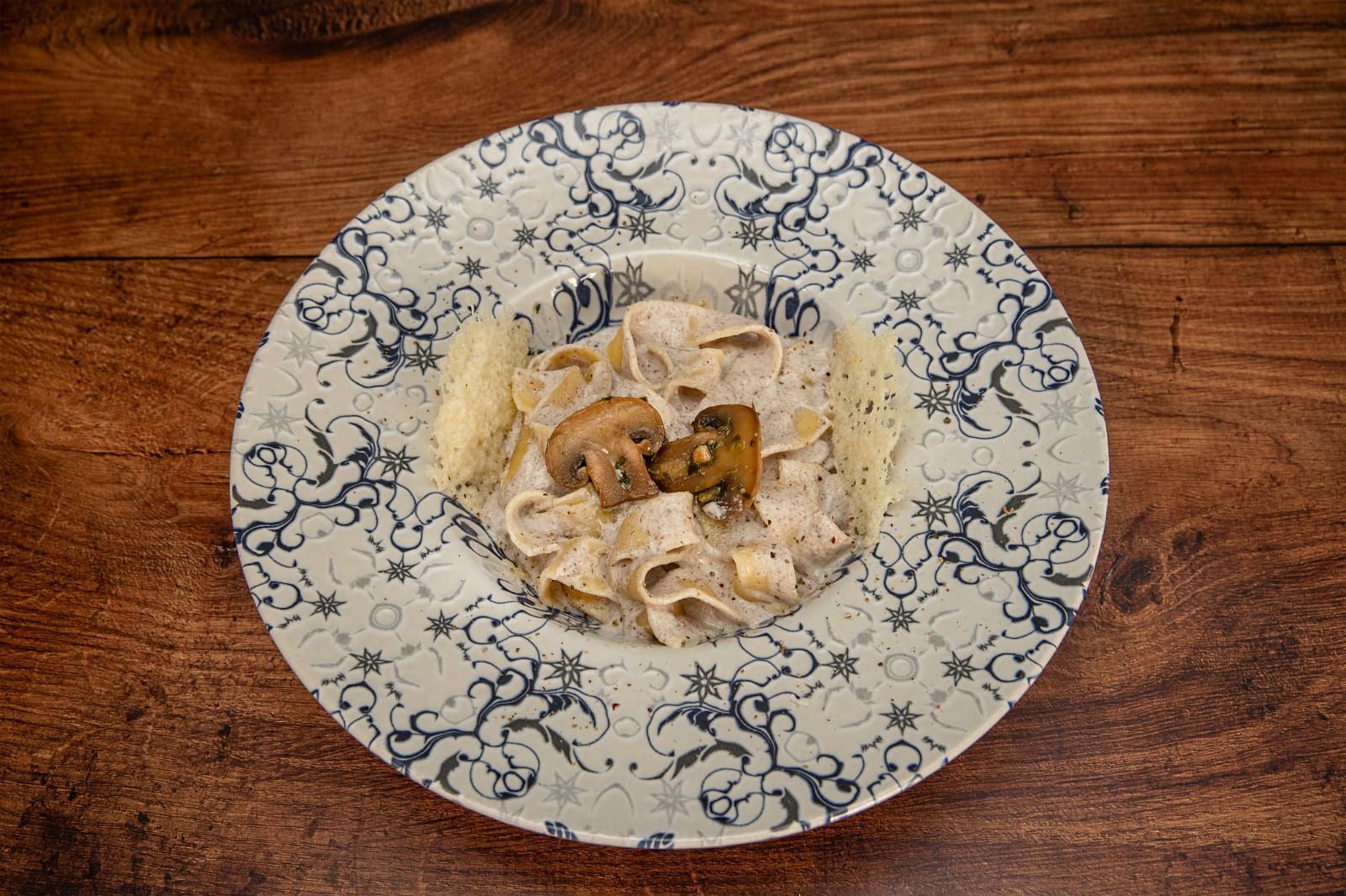 Plato de pasta con setas, servido en un plato estampado, sobre una mesa de madera.