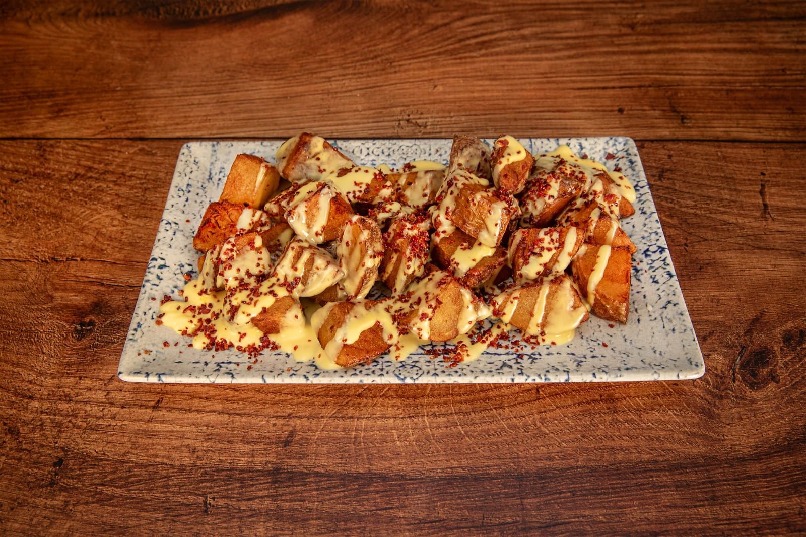 Patatas fritas con salsa y chispitas de colores sobre un plato rectangular, sobre un fondo de madera.