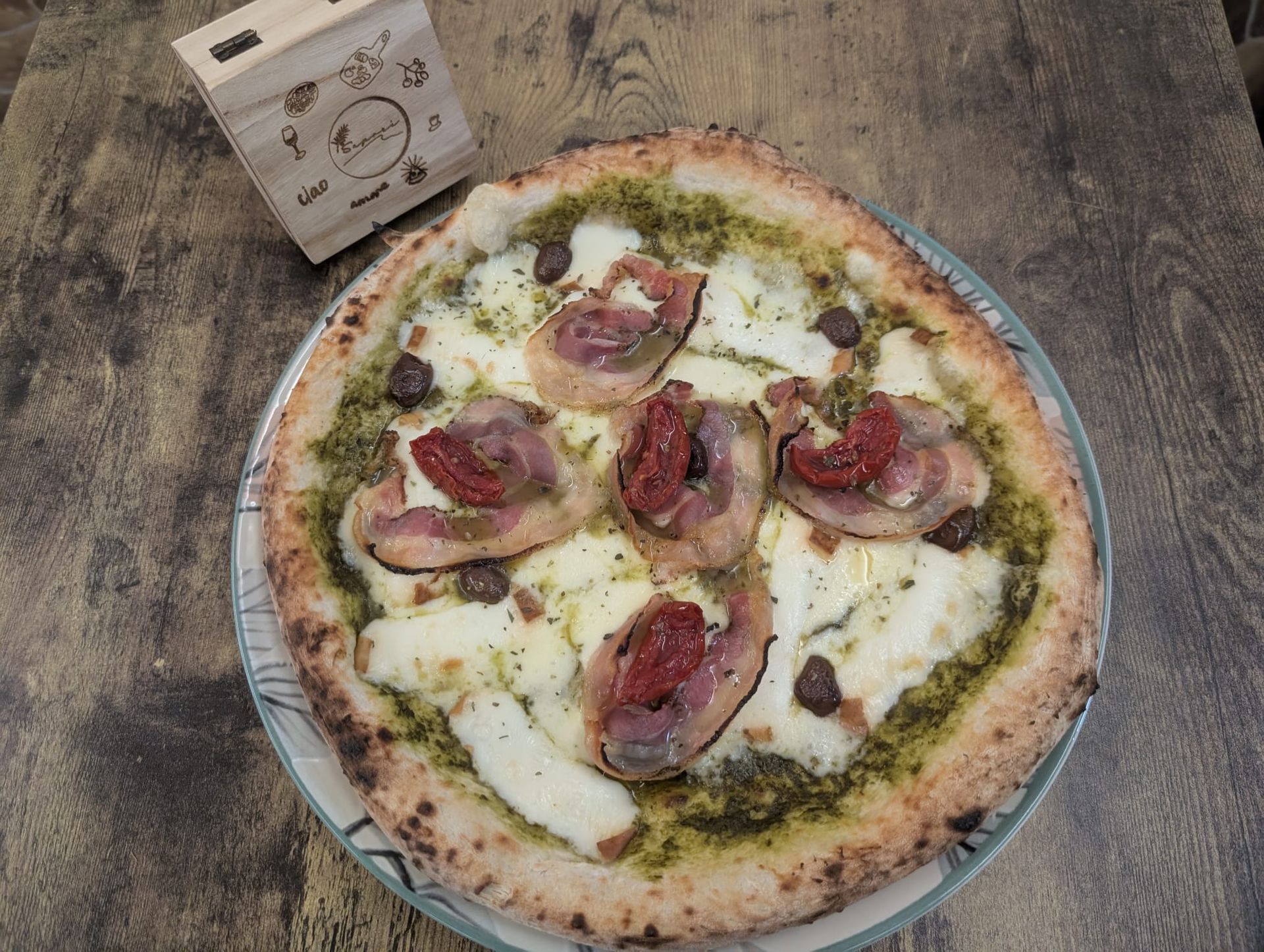 Pizza con pesto, queso, embutidos y tomates secos en un plato, sobre una mesa de madera.