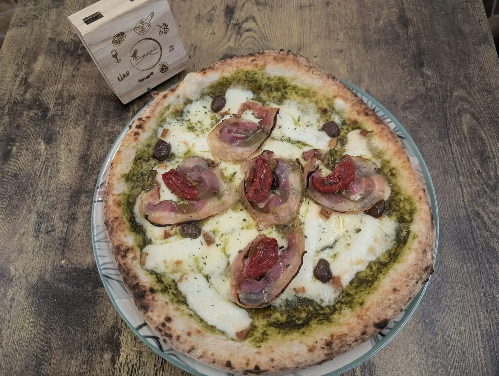 Pizza en plato, con pesto, queso, embutidos y tomates secos.