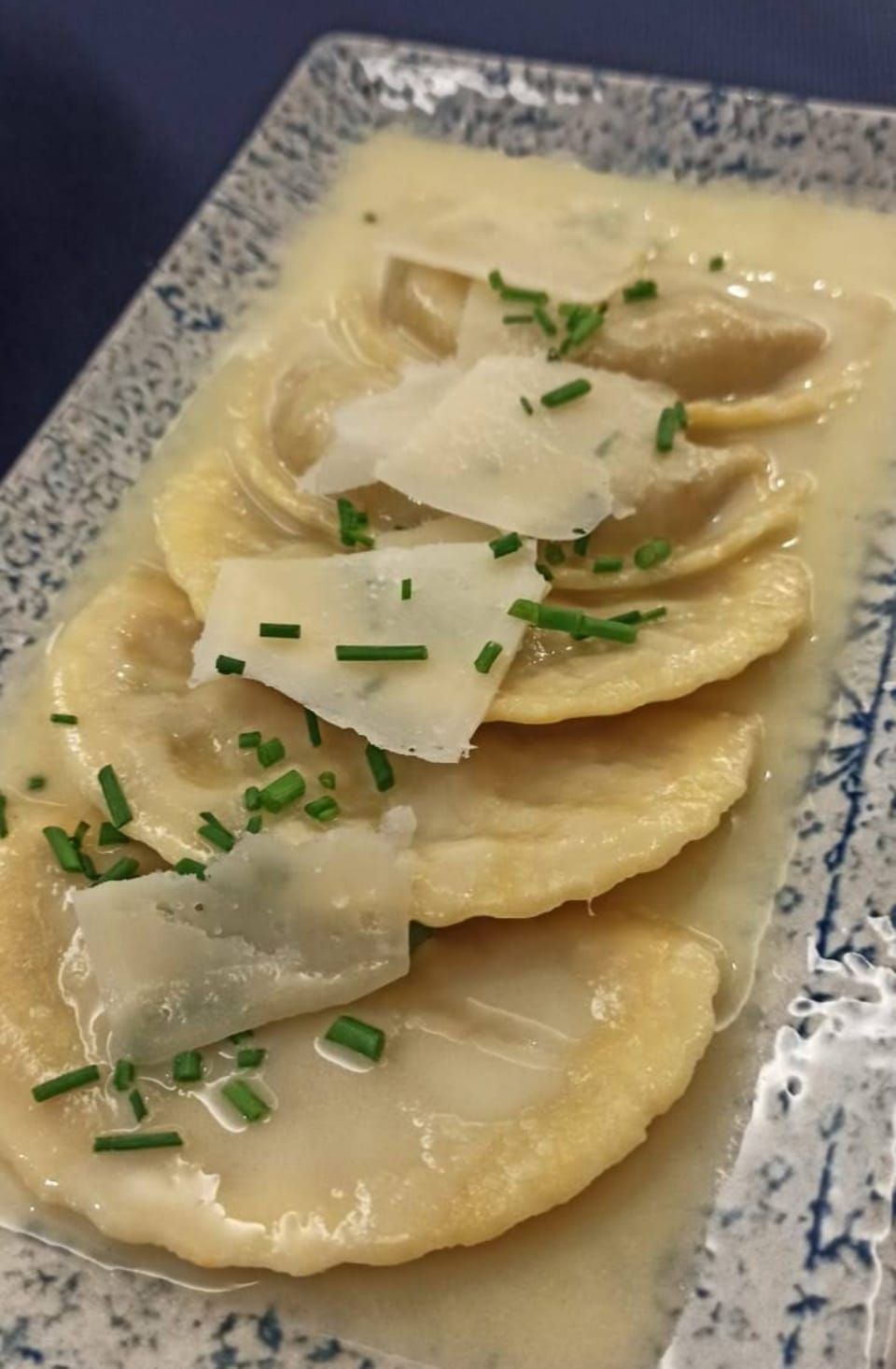 Pasta ravioles en salsa cremosa, cubiertos con queso rallado y cebollino en un plato estampado.